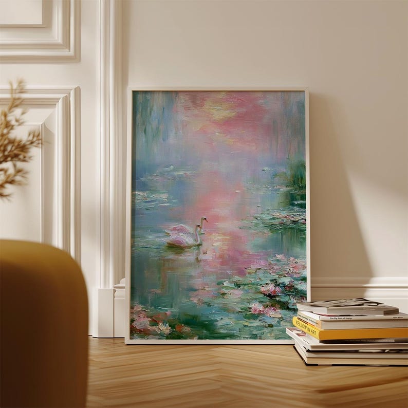 May include: Framed artwork depicting a serene lake scene with two swans. The painting features a soft color palette of pink, blue, and green, with lily pads and reflections in the water. The artwork is leaning against a white wall.