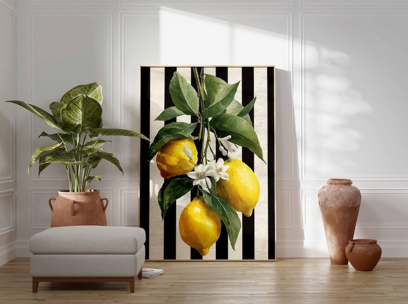 May include: A framed art print featuring a vibrant lemon branch with bright yellow fruit and green leaves against a black and white striped background. The artwork includes white blossoms and is displayed in a room with a potted plant and a neutral-toned ottoman.