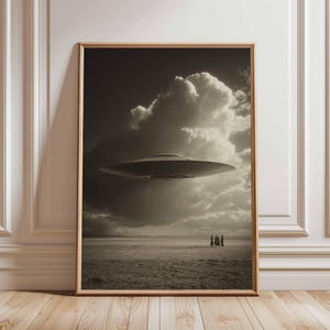 May include: Sepia-toned framed print depicting a UFO above a desert scene with a cloudy sky. A group of figures are seen in the distance. The artwork is displayed against a white wall and wooden floor.