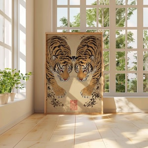 May include: A framed artwork featuring two tigers facing each other. The tigers have orange and black stripes with detailed fur patterns. The artwork is set against a light beige background, with a wooden frame. The image is displayed in a room with natural light.