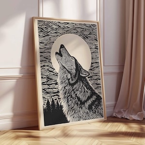 May include: A framed black and white art print depicting a howling wolf under a full moon. The woodcut-style artwork shows detailed lines. The background features stylized clouds and a silhouetted forest. The frame is a light wood colour.
