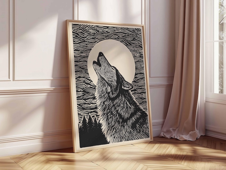 May include: A framed black and white art print depicting a howling wolf under a full moon. The woodcut-style artwork shows detailed lines. The background features stylized clouds and a silhouetted forest. The frame is a light wood colour.