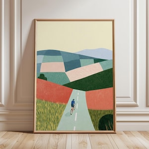 May include: Art print in a wooden frame showing a cyclist on a road through a patchwork landscape. The illustration uses greens, blues, pinks, and reds, with a pale yellow sky. The cyclist is in blue, creating a focal point in the artwork.