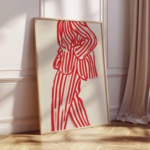 K&ouml;nnte beinhalten: Ein gerahmter Kunstdruck mit einer rot-wei&szlig; gestreiften Figur. Das Kunstwerk zeigt eine Person in einem Anzug mit kr&auml;ftigen vertikalen Streifen. Der Druck wird vor einem neutralen Hintergrund gezeigt, der an einer wei&szlig;en Wand und einem Holzboden lehnt.