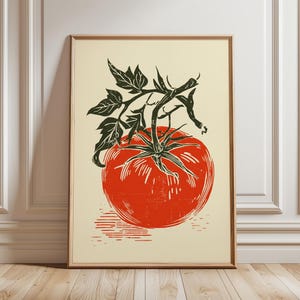 Könnte beinhalten: Gerahmter Kunstdruck mit einer leuchtend roten Tomate mit grünen Blättern und Stiel. Die Tomatenillustration befindet sich vor einem cremefarbenen Hintergrund, in einem Holzrahmen. Das Kunstwerk ist ein Druck im Linolschnittstil.