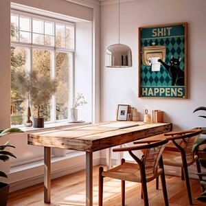 May include: A framed poster with the text "SHIT HAPPENS" and a cartoon cat reaching for toilet paper hangs above a wooden desk. The room features a large window, a pendant light, and two woven chairs.