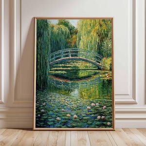 Puede incluir: Una impresión artística enmarcada de una serena escena de jardín acuático. La pintura representa un puente verde arqueado sobre un estanque lleno de nenúfares y flores rosas. Frondosos árboles verdes y sus reflejos completan el tranquilo paisaje.