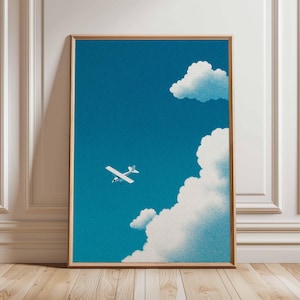 Op de afbeelding: Een ingelijste kunstdruk met een klein wit vliegtuig dat door een helderblauwe lucht vliegt, bezaaid met pluizige witte wolken. Het kunstwerk heeft een getextureerde, korrelige uitstraling en is gevat in een houten lijst.
