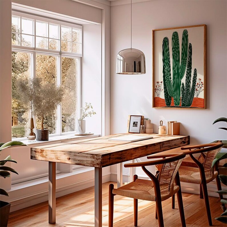 May include: A bright, airy room with a wooden desk and two chairs. A large framed print of green cacti hangs on the wall. A large window offers a view of trees. A silver pendant light hangs above the desk.