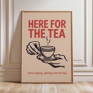 以下が含まれることがあります： 赤い文字で「HERE FOR THE TEA」と書かれた額入りのポスター。テキストの下には、ティーカップとソーサーを持った手の白黒イラストがあります。ポスターの下部には「more sipping, spilling and stirring」と書かれています。