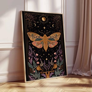 May include: Framed art print featuring a large moth with intricate wing patterns in shades of orange, green, and pink against a black background. The artwork includes celestial elements like moons and stars, and floral accents. The frame is gold.