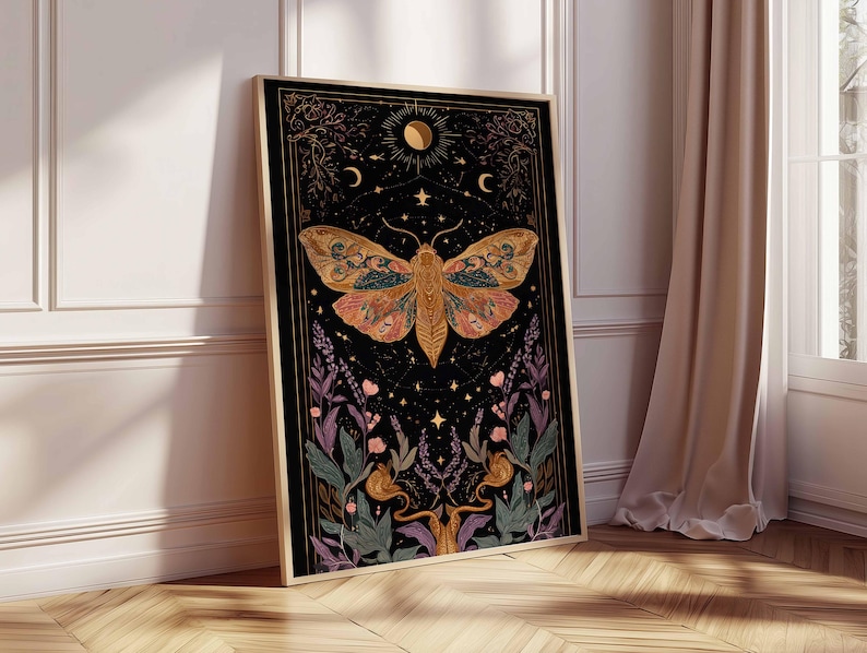 May include: Framed art print featuring a large moth with intricate wing patterns in shades of orange, green, and pink against a black background. The artwork includes celestial elements like moons and stars, and floral accents. The frame is gold.