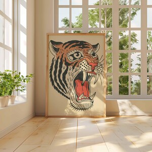 May include: A framed illustration of a tiger's head with an open mouth, showcasing sharp teeth and a red interior. The tiger has orange and black stripes, set against a cream background. The artwork is displayed in a room with a window and plants.