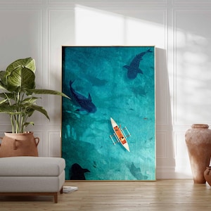 May include: An art print featuring an aerial view of the ocean with large dark blue whale sharks swimming beneath the surface. A small white boat with orange accents floats on the turquoise water. The artwork is framed in a gold border.