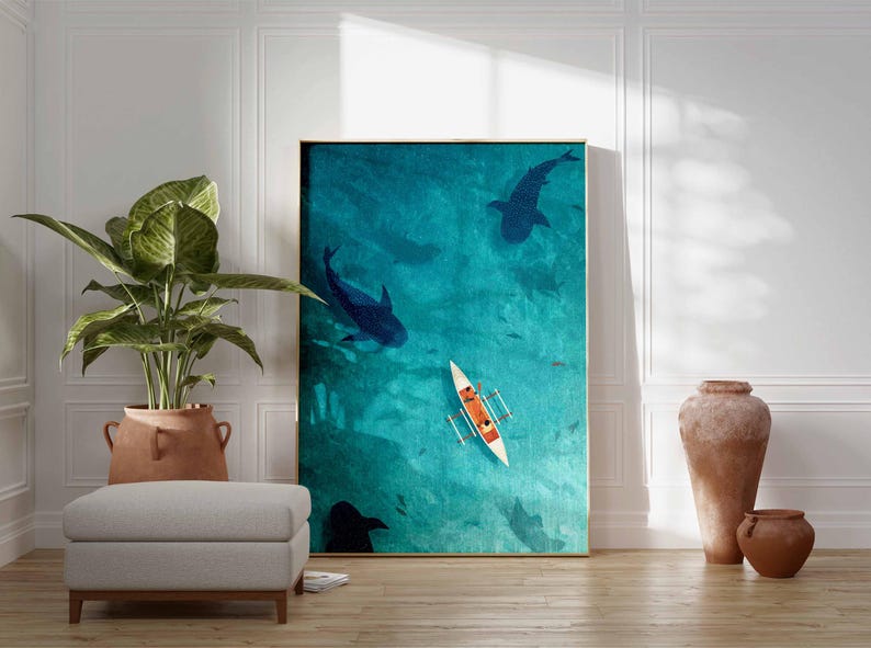 May include: An art print featuring an aerial view of the ocean with large dark blue whale sharks swimming beneath the surface. A small white boat with orange accents floats on the turquoise water. The artwork is framed in a gold border.