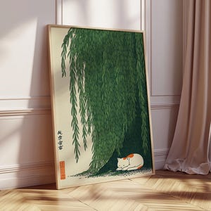 May include: A framed art print featuring a Japanese-style illustration. The artwork depicts a green weeping willow tree with a white and orange cat resting beneath its branches. The print has Japanese text and a red seal.