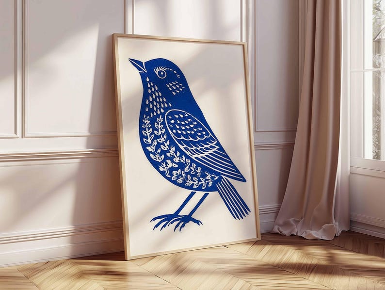 May include: A framed art print featuring a stylized blue bird illustration. The bird is depicted with intricate white floral patterns on its body and wings. The artwork is set against a cream background, with a wooden frame.