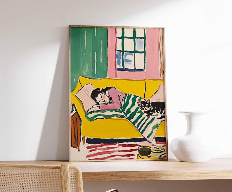 May include: A painting of a woman sleeping on a yellow sofa with a black cat curled up on the blanket. The sofa is in a room with a pink wall and a green curtain. The painting is framed in a wooden frame.