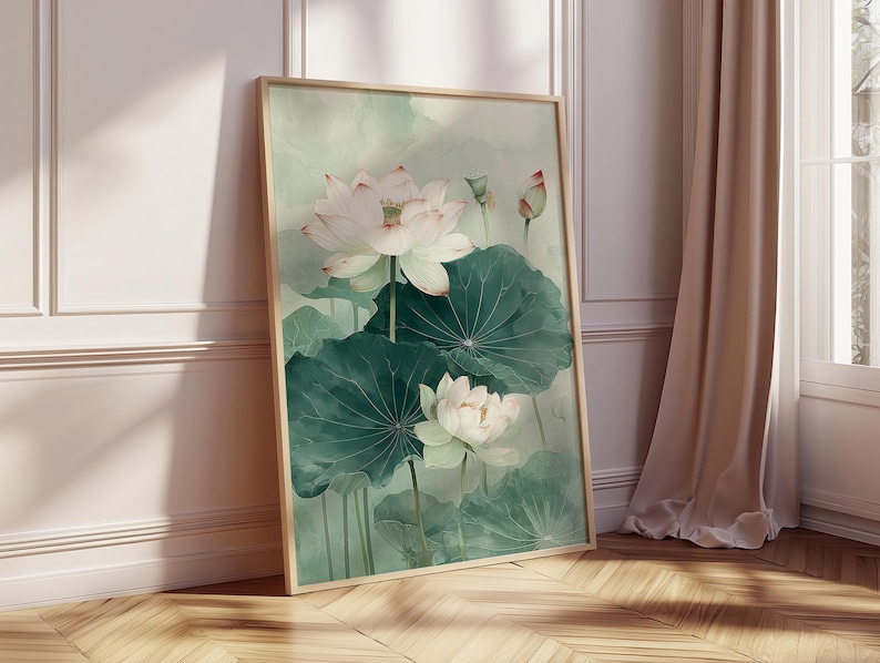 Puede incluir: Una impresi&oacute;n en acuarela enmarcada con flores de loto blancas y hojas verdes. La obra de arte tiene una paleta de colores suaves y apagados con un marco de madera clara. La impresi&oacute;n est&aacute; apoyada contra una pared.