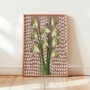Op de afbeelding: Een ingelijste rechthoekige wandkunstprint met een botanische illustratie van verschillende hangende klokvormige bloemen met groen-witte stippenpatronen. De achtergrond is een effen gedempte bruine kleur met een herhalend patroon van witte ovalen.