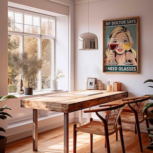 May include: A room with a wooden table and two chairs. A poster on the wall reads "MY DOCTOR SAYS I NEED GLASSES" and depicts a woman holding wine glasses. A large window offers a view of trees.