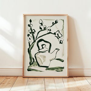Op de afbeelding: Een ingelijste kunstdruk met een minimalistische inktillustratie van een theepot onder een bloeiende tak. Het kunstwerk gebruikt donkergroene penseelstreken op een lichtcrème achtergrond, gevat in een eenvoudige lijst van licht hout.