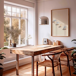 May include: A light and airy room featuring a wooden desk and two chairs. A framed print of a beach scene hangs on the wall. A large window offers a view of trees. A silver pendant light hangs above the desk.