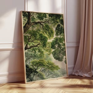 May include: A framed art print featuring a watercolor painting of a forest canopy. The artwork showcases lush green foliage and tree branches, with a soft, diffused light filtering through. The frame is a light wood color, and the print is leaning against a wall.