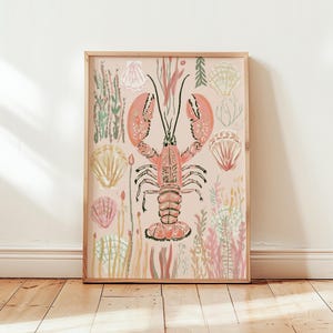 May include: A rectangular wall art print in a light wood frame featuring a central illustration of a coral-colored lobster surrounded by various seashells and seaweed in soft pastel shades of pink, green, and cream on a light beige background.