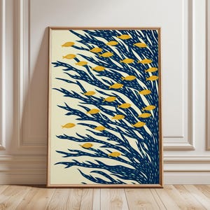 May include: A framed art print depicting yellow fish swimming through blue seaweed on a cream backdrop. The artwork has a minimalist, illustrative style, suitable for coastal decor. The frame is a warm, natural wood.