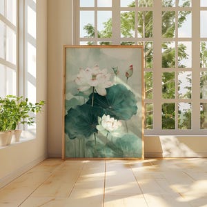 Puede incluir: Una impresi&oacute;n art&iacute;stica enmarcada que presenta una pintura de acuarela de flores de loto blancas con grandes hojas verdes. La obra de arte se exhibe en una habitaci&oacute;n soleada con piso de madera y una ventana con vista a un paisaje verde.