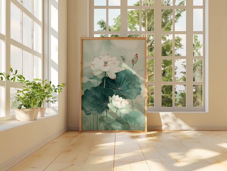 Puede incluir: Una impresi&oacute;n art&iacute;stica enmarcada que presenta una pintura de acuarela de flores de loto blancas con grandes hojas verdes. La obra de arte se exhibe en una habitaci&oacute;n soleada con piso de madera y una ventana con vista a un paisaje verde.