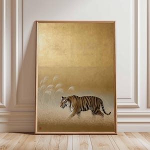 May include: A framed art print featuring a tiger walking through tall grass. The artwork has a gold background with a textured appearance. The tiger is depicted with brown and black stripes, and the frame is a light wood color.