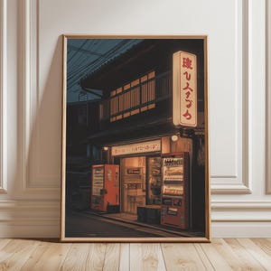 以下が含まれることがあります： 夜の日本の街並みの額装プリント。自動販売機と日本語の看板があるお店が写っています。温かい光で照らされ、居心地の良い雰囲気を作り出しています。木製のフレームに入っています。