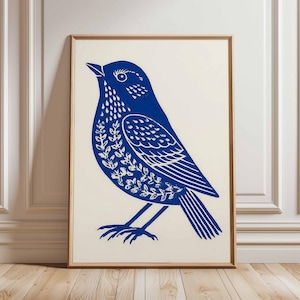 May include: A framed print featuring a stylized blue bird illustration. The bird is depicted with intricate details, including leaf-like patterns on its chest and wings. The artwork is set against a cream-colored background and framed in a wooden frame.