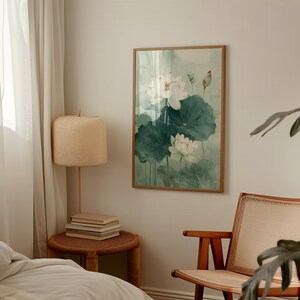 Puede incluir: Una pintura de acuarela enmarcada de flores de loto blancas y hojas verdes grandes. La obra de arte tiene una paleta de colores suaves y apagados con un fondo verde claro. La pintura se exhibe en una habitaci&oacute;n con una combinaci&oacute;n de colores neutros.