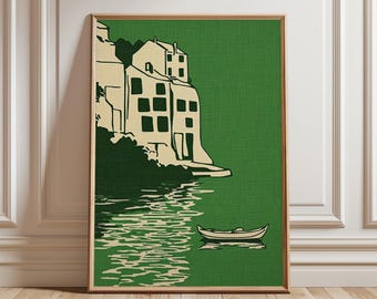 Puede incluir: Un grabado enmarcado que representa una escena costera. La obra de arte muestra edificios en un acantilado, en crema sobre un fondo verde. Un pequeño bote flota en el agua debajo. El grabado está enmarcado en madera.