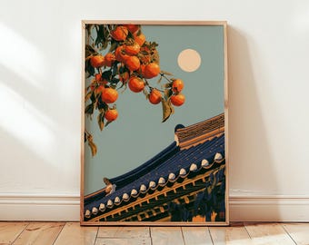 Puede incluir: Una lámina enmarcada que muestra una rama de caquis de color naranja brillante sobre el tejado de tejas azul oscuro de un edificio tradicional. Una luna circular de color amarillo pálido se ve en el cielo verde salvia sobre la estructura.