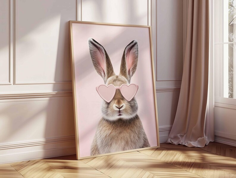 May include: A framed print featuring a close-up of a rabbit wearing pink heart-shaped sunglasses. The rabbit has brown and tan fur with long ears. The background is a soft pink color.