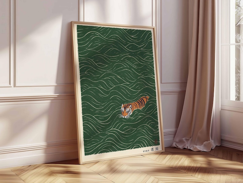 May include: Framed art print featuring a tiger swimming in green water with white wave patterns. The tiger has orange and black stripes. The artwork is in a wooden frame and leans against a white wall and wooden floor.