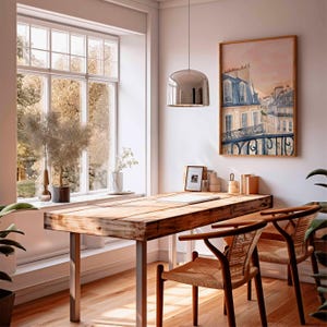May include: A light-filled room featuring a wooden desk and two chairs. A framed painting of a European cityscape adorns the wall. A large window provides a view of trees. A silver pendant light hangs above the desk.