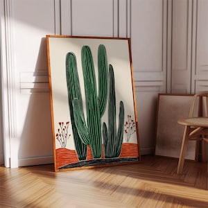 May include: A framed art print featuring a stylized illustration of green cacti against a cream background. The cacti are set on an orange and black ground, with small red floral accents. The frame is a warm brown color.