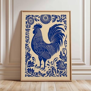 以下が含まれることがあります： 青い雄鶏のイラストが描かれたフレーム入りプリント。雄鶏は、クリーム色の背景に、補色である青色の花のボーダーで囲まれています。このアートワークは木製のフレームに収められています。