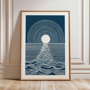 Puede incluir: Una impresión artística enmarcada con un diseño minimalista de un sol poniéndose sobre el océano. La obra de arte utiliza líneas blancas sobre un fondo azul oscuro para representar el reflejo del sol en el agua. La impresión está en un marco de madera.