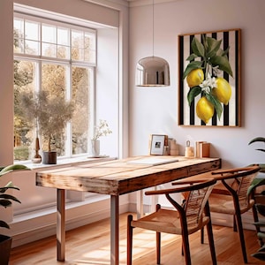 May include: A bright, airy interior with a wooden desk and two chairs. A framed artwork of lemons hangs on the wall with a black and white striped background. A large window offers a view of the outdoors, and a modern light fixture hangs from the ceiling.