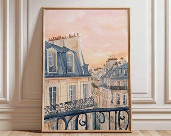 Op de afbeelding: Aquarel schilderij van Parijse gebouwen met blauwe daken en een smeedijzeren balkon. Het kunstwerk is ingelijst in een lichtbruine houten lijst. De lucht is zachtroze en oranje, wat duidt op een zonsondergang of zonsopgang.