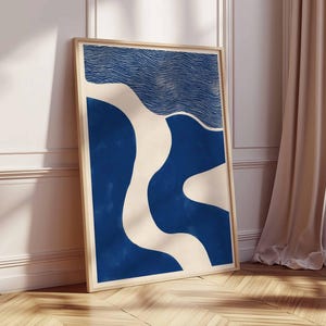 Puede incluir: Un cuadro enmarcado con arte abstracto en tonos azul y crema. La obra presenta un patr&oacute;n ondulado con un dise&ntilde;o lineal texturizado en la parte superior. El marco es de madera clara y la impresi&oacute;n se apoya en una pared blanca. Medidas: aprox. 60 cm x 90 cm.