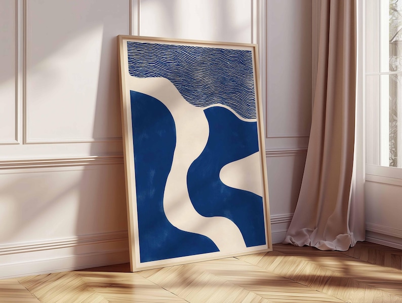 Puede incluir: Un cuadro enmarcado con arte abstracto en tonos azul y crema. La obra presenta un patr&oacute;n ondulado con un dise&ntilde;o lineal texturizado en la parte superior. El marco es de madera clara y la impresi&oacute;n se apoya en una pared blanca. Medidas: aprox. 60 cm x 90 cm.