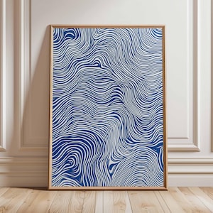 Könnte beinhalten: Ein gerahmter Kunstdruck mit einem blauen und weißen Wellenmuster. Das Kunstwerk wird in einem hellbraunen Holzrahmen präsentiert und lehnt an einer weißen Wand und einem Holzboden.