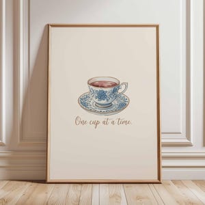 May include: Framed print with a watercolour illustration of a teacup and saucer, both adorned with blue floral patterns. The teacup contains tea. The text "One cup at a time" is below the teacup.